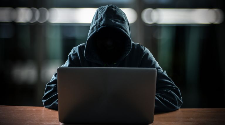 Hooded cyber criminal sitting at his laptop.